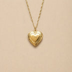 Zoom sur le collier Précieux, médaillon cœur en acier doré avec gravure et  photo souvenir à personnaliser, posé sur un fond beige texturé.