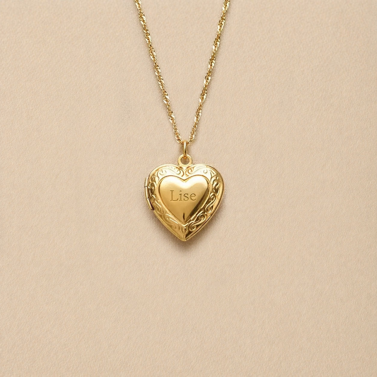 Zoom sur le collier Précieux, médaillon cœur en acier doré avec gravure et  photo souvenir à personnaliser, posé sur un fond beige texturé.