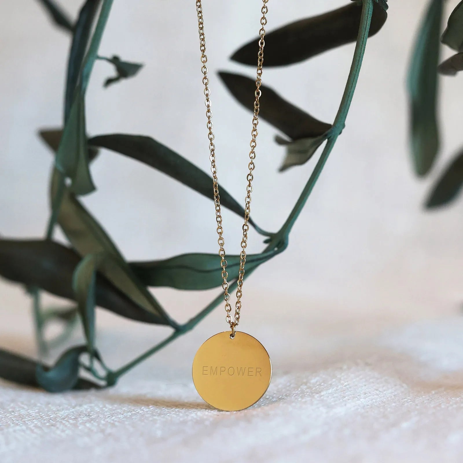 Collier Renaissance doré, médaille ronde martelée à graver vue de dos, suspendue sur une branche de feuilles. 