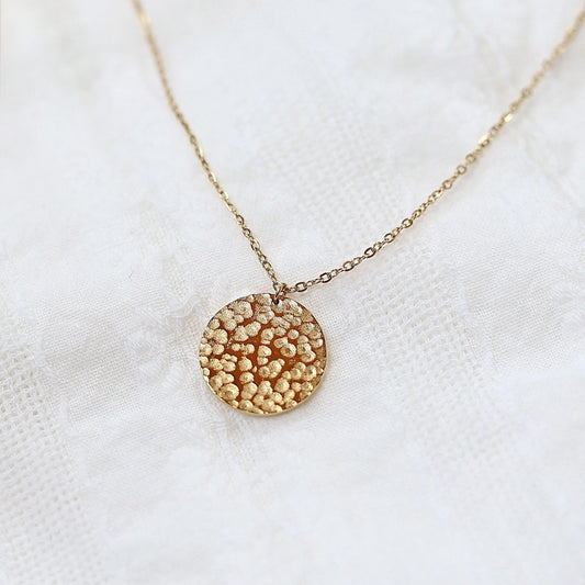 Collier Renaissance doré, médaille ronde martelée personnalisable au dos, délicatement posé sur un tissu beige. 