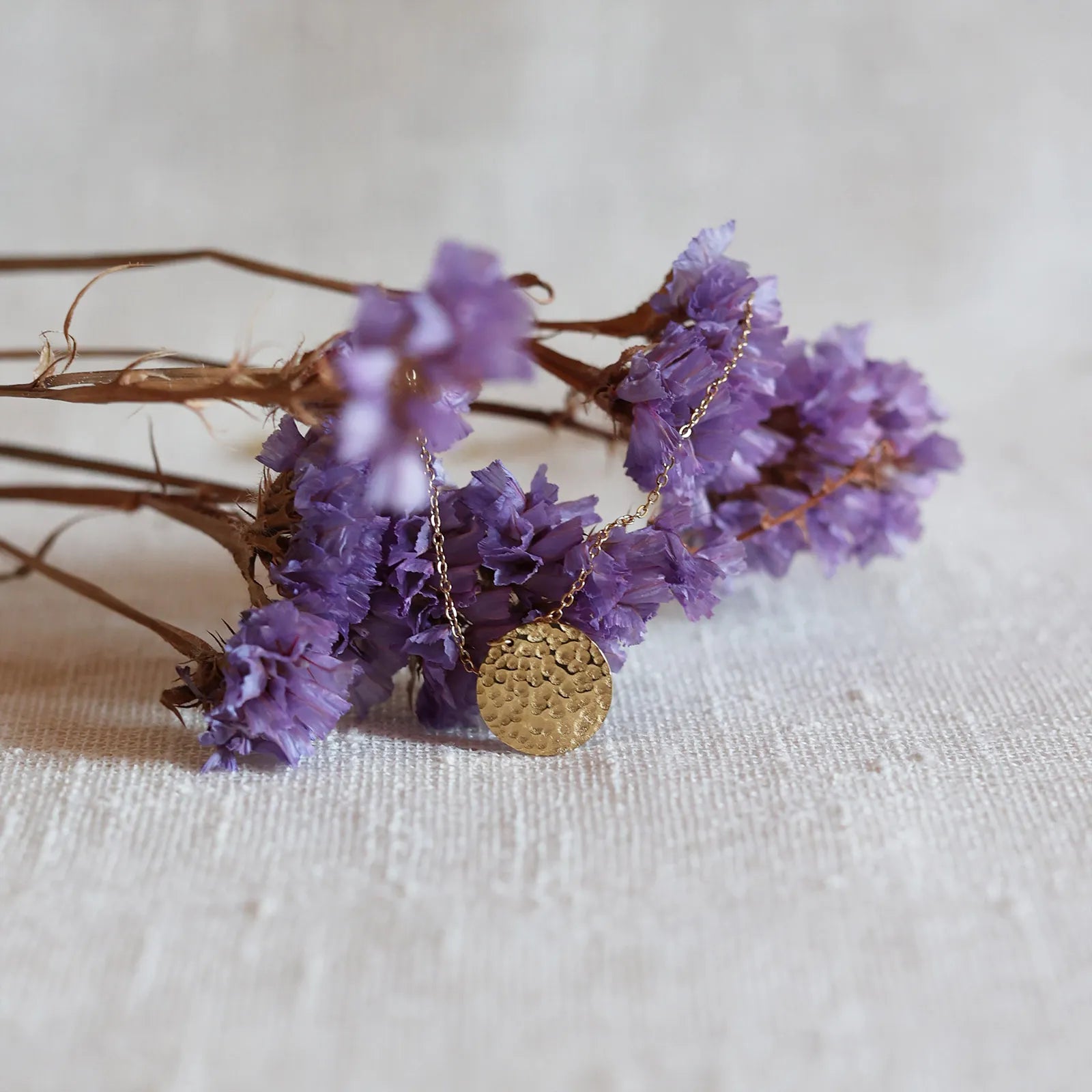 Collier Renaissance doré, médaille ronde martelée à graver vue de face, suspendue sur des fleurs violettes. 