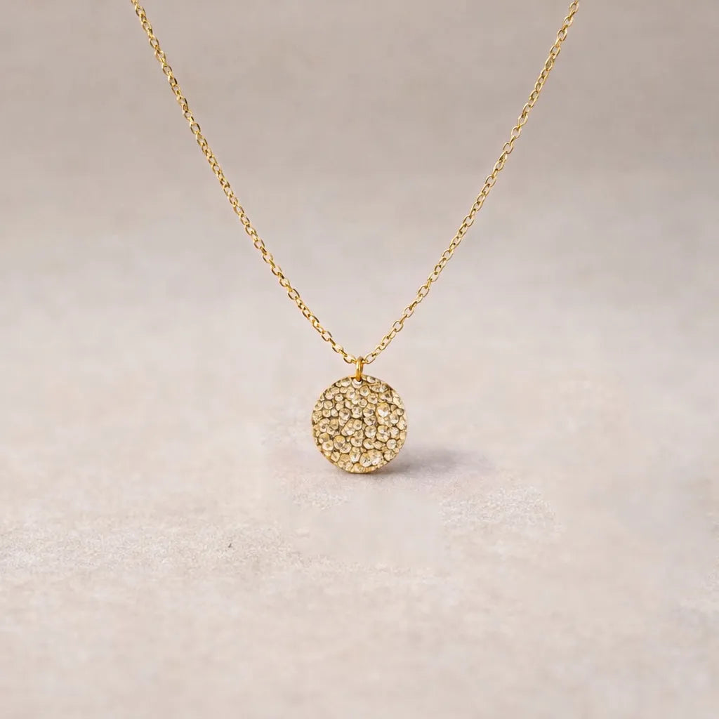 Collier Renaissance doré, médaille ronde martelée à graver vue de face, posé sur fond beige texturé.