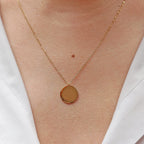 Collier "Reflet" avec médaille ronde personnalisé en acier inoxydable doré, porté autour du cou.