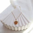 Collier "Ce jour là" avec médaillon rond personnalisable en acier doré, présenté sur un fond beige texturé.