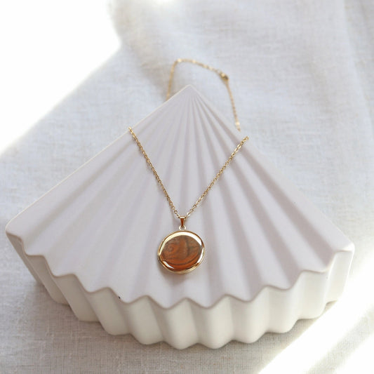 Collier "Ce jour là" avec médaillon rond personnalisable en acier doré, présenté sur un fond beige texturé.