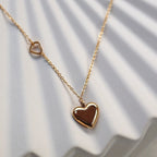 Zoom sur le collier "Ma vie" en acier doré, avec pendentif cœur personnalisable et petit coeur sur la chaîne, posé sur fond beige. 