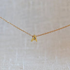 Collier L'instant avec pendentif lettre A en acier inoxydable doré, bijou minimaliste suspendu sur fond beige.