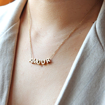 Collier L'instant avec lettres AMOUR dorées, en acier inoxydable, porté au cou.