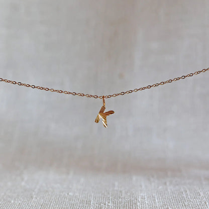 Collier "Je suis" avec pendentif lettre K striée en acier doré, suspendu sur un fond en tissu beige texturé.
