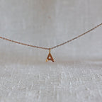 Collier "Je suis" avec pendentif lettre A striée en acier doré, suspendu sur un fond en tissu beige texturé.