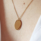 Zoom sur le collier "Tendresse", pendentif ovale personnalisable en acier inoxydable doré, porté autour du cou.