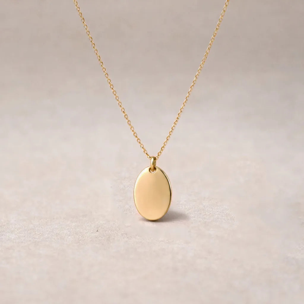 Collier "Tendresse", pendentif ovale personnalisable en acier inoxydable argenté, présenté sur un fond beige texturé.