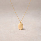 Collier "Tendresse", pendentif ovale personnalisable en acier inoxydable argenté, présenté sur un fond beige texturé.