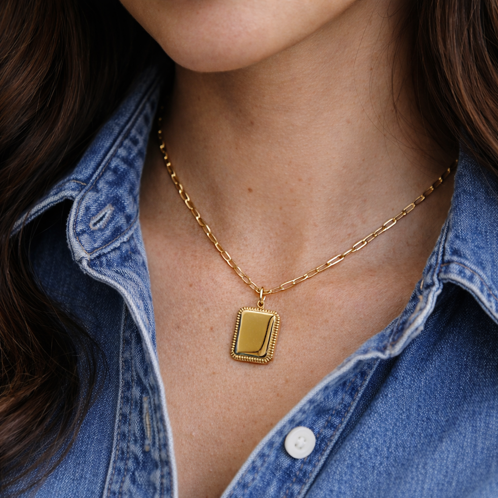 Collier Trésor avec pendentif rectangulaire personnalisable en acier doré, porté autour du cou d'une jeune femme qui porte une chemise jeans bleu.