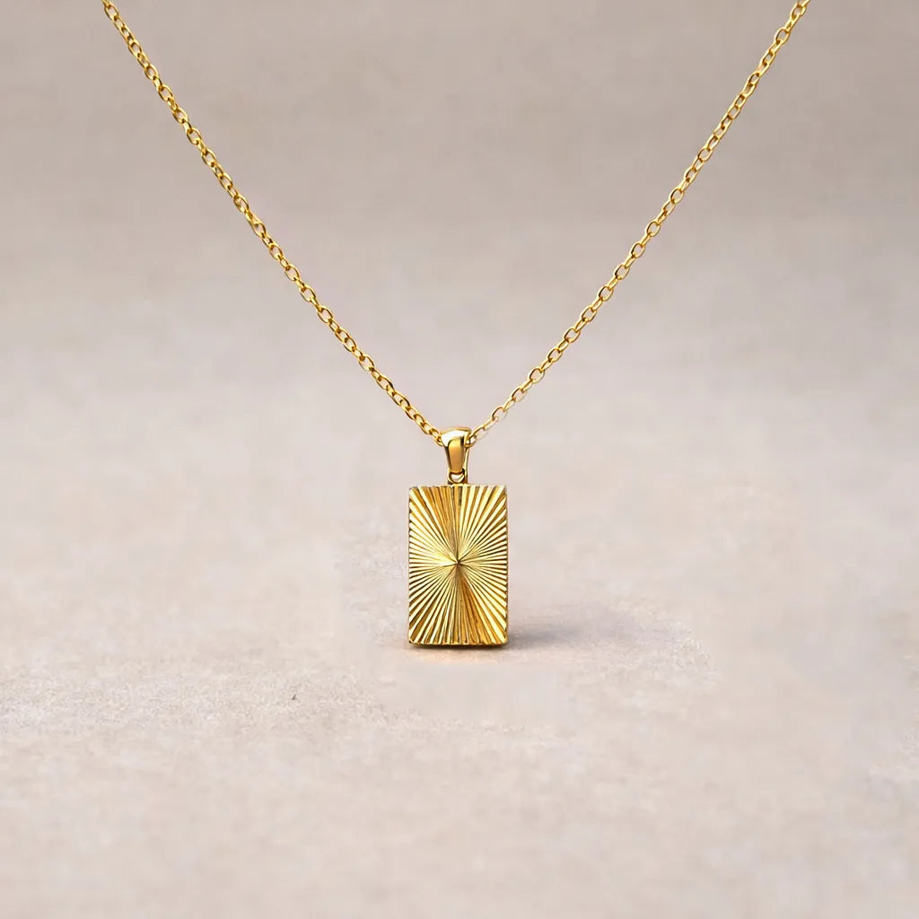Collier Eclat  en acier doré avec pendentif rectangulaire gravé de rayons, personnalisable au verso, vue de face sur support beige texturé.