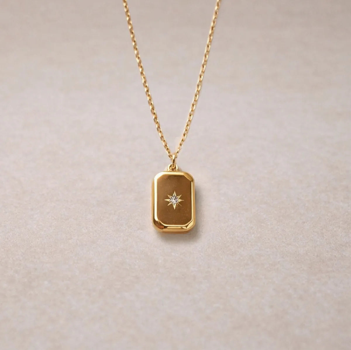 Collier Horizon avec pendentif rectangulaire personnalisable en acier doré, sur fond beige texturé.