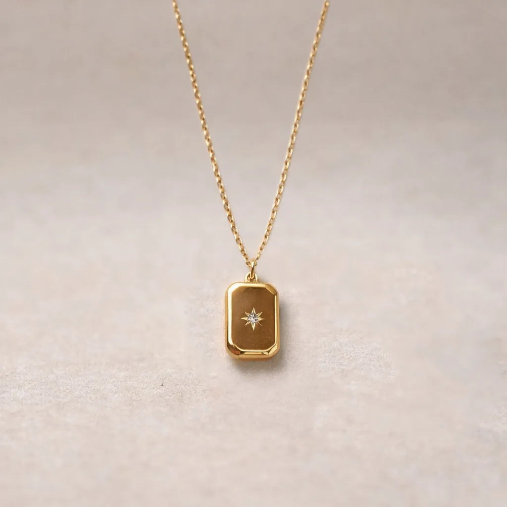 Collier Horizon avec pendentif rectangulaire personnalisable en acier doré, sur fond beige texturé.