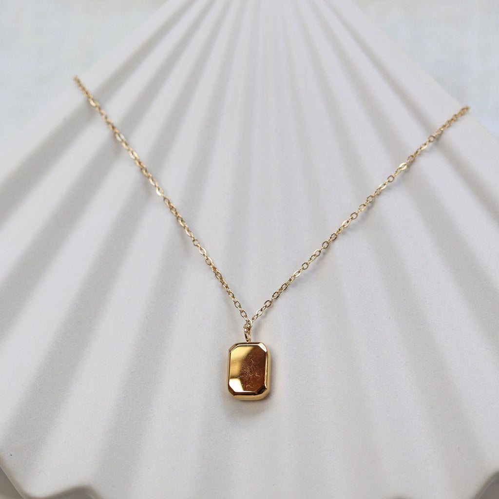 Collier "Ma voie" avec pendentif rectangulaire en acier doré, vue de dos personnalisable sur fond beige texturé.