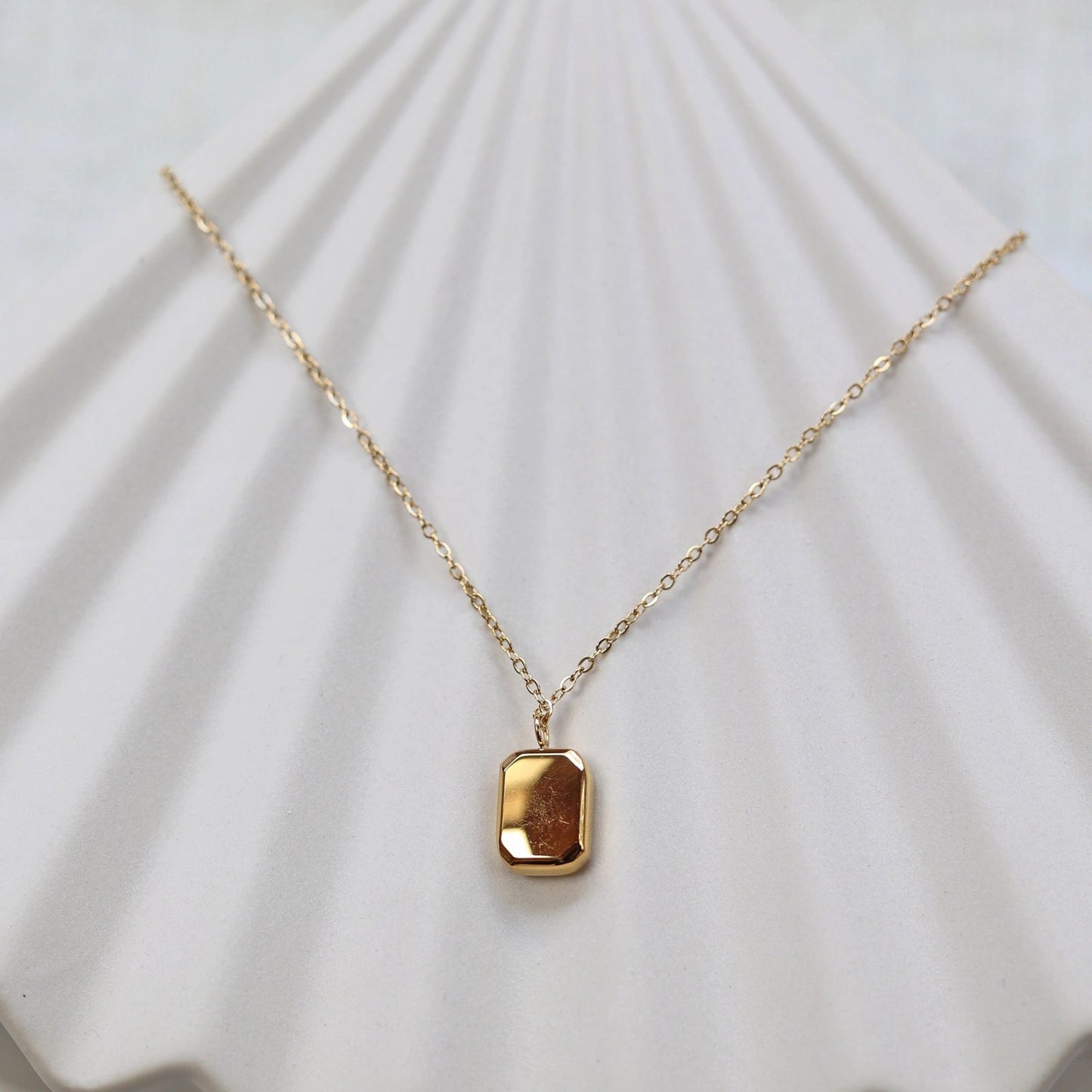 Collier "Ma voie" avec pendentif rectangulaire en acier doré, vue de dos personnalisable sur fond beige texturé.