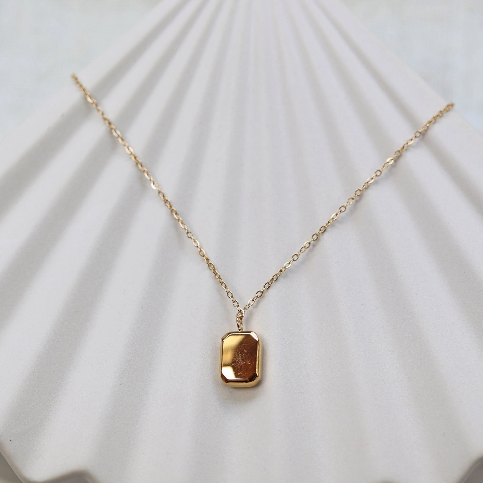 Collier "Ma voie" avec pendentif rectangulaire en acier doré, vue de dos personnalisable sur fond beige texturé.