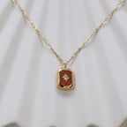 Collier "Ma voie" avec pendentif rectangulaire personnalisable en acier doré, sur fond beige texturé.