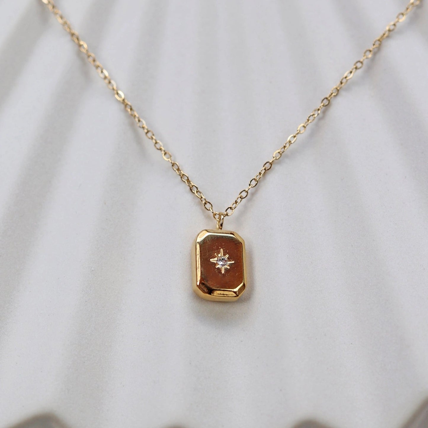 Collier "Ma voie" avec pendentif rectangulaire personnalisable en acier doré, sur fond beige texturé.
