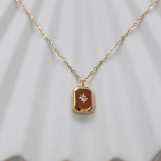 Collier "Ma voie" avec pendentif rectangulaire personnalisable en acier doré, sur fond beige texturé.