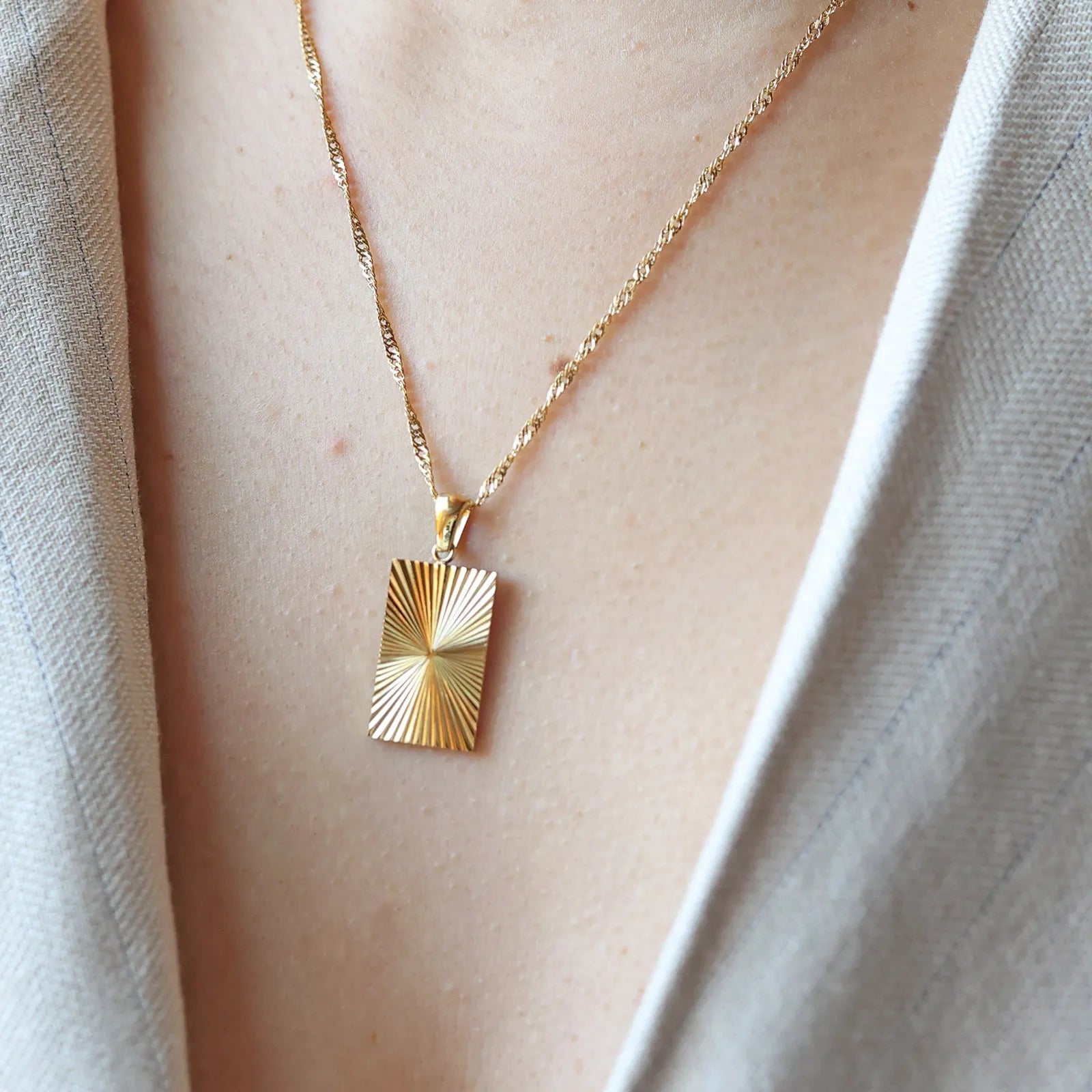 Collier Résilience en acier doré avec pendentif rectangulaire gravé de rayons, personnalisable au verso, porté autour du cou.