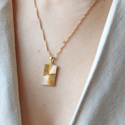 Collier Résilience en acier doré avec pendentif rectangulaire gravé de rayons, personnalisable au verso, porté autour du cou.