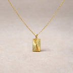 Collier Résilience en acier doré avec pendentif rectangulaire gravé de rayons, personnalisable au verso, vue de face sur support beige texturé.