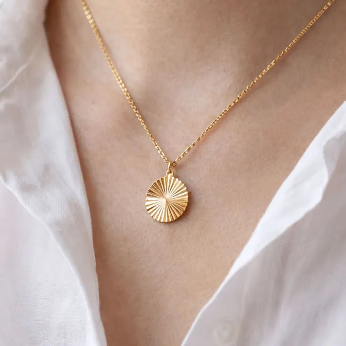 Collier "Energie" avec pendentif rond strié personnalisé en acier doré, porté autour du cou.