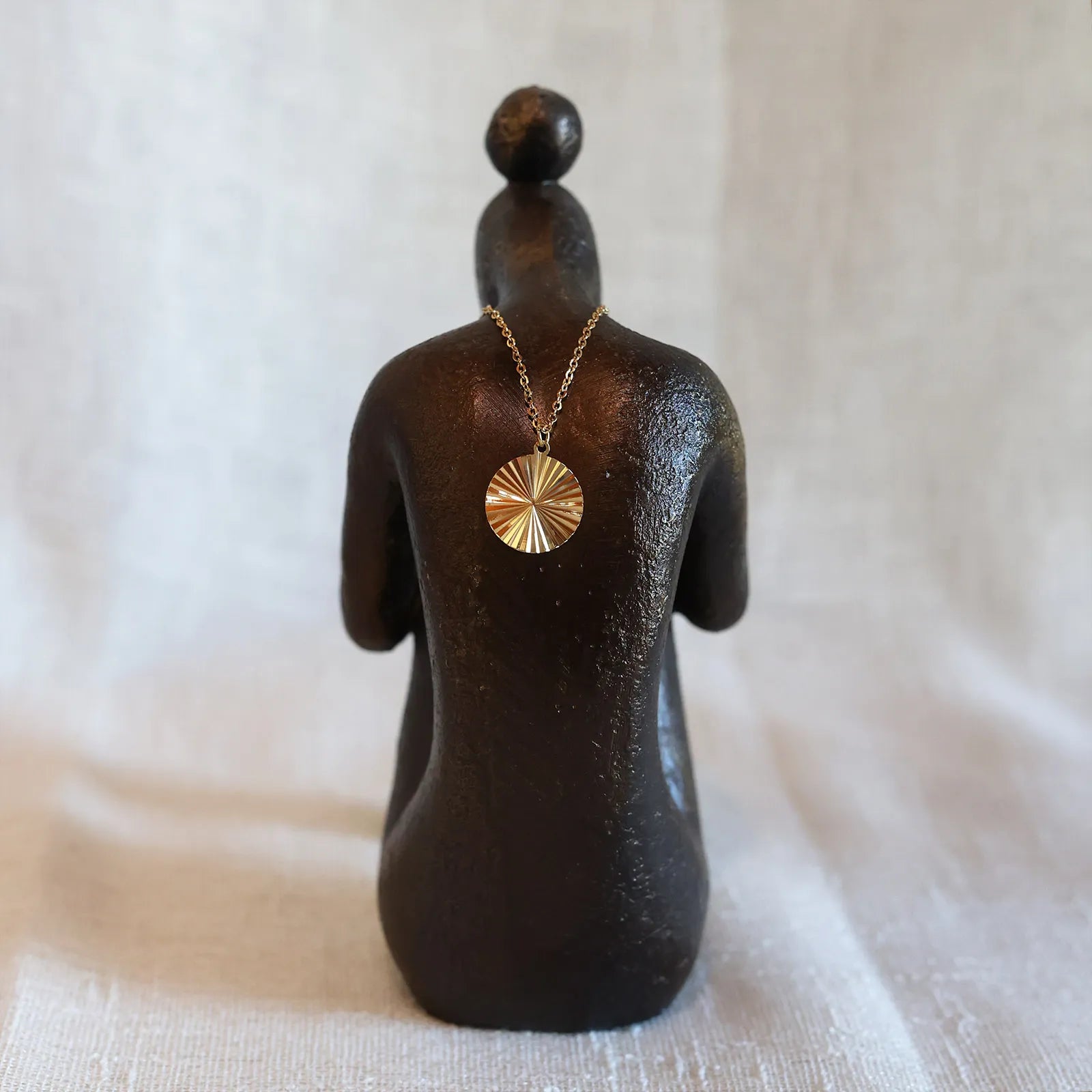 Vue arrière du collier "Energie", pendentif rond strié personnalisable en acier doré, posé sur une statue de femme de dos.