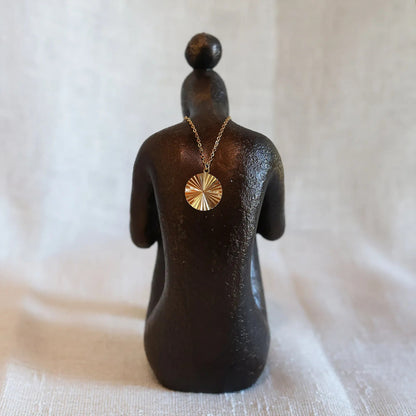 Vue arrière du collier "Energie", pendentif rond strié personnalisable en acier doré, posé sur une statue de femme de dos.