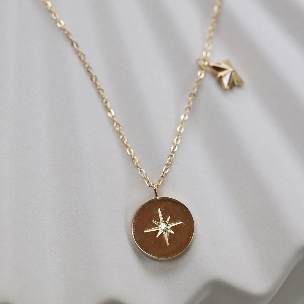 Collier Mon rêve en acier doré avec pendentif rond orné d'une étoile et d'un zircon, présenté face visible sur un fond beige. Verso personnalisable - Visée Bijoux.
