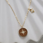 Collier Mon rêve en acier doré avec pendentif rond orné d'une étoile et d'un zircon, présenté face visible sur un fond beige. Verso personnalisable - Visée Bijoux.