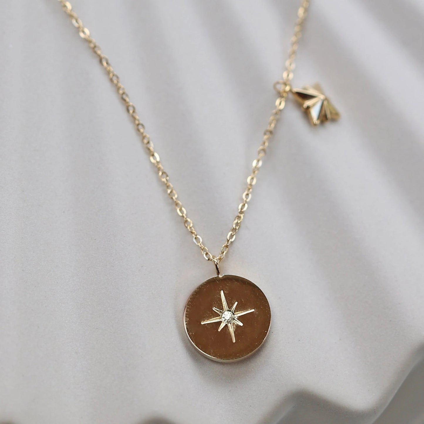 Collier Mon rêve en acier doré avec pendentif rond orné d'une étoile et d'un zircon, présenté face visible sur un fond beige. Verso personnalisable - Visée Bijoux.