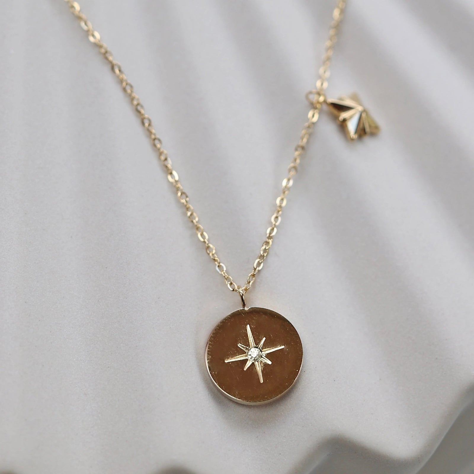 Collier Mon rêve en acier doré avec pendentif rond orné d'une étoile et d'un zircon, présenté face visible sur un fond beige. Verso personnalisable - Visée Bijoux.
