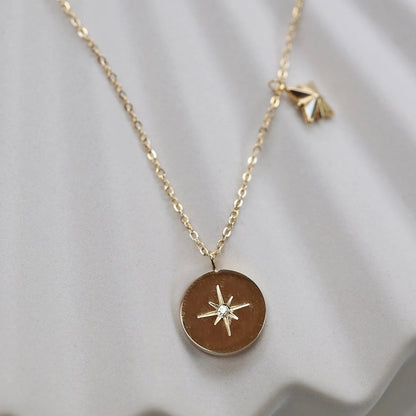 Collier Mon rêve en acier doré avec pendentif rond orné d'une étoile et d'un zircon, présenté face visible sur un fond beige. Verso personnalisable - Visée Bijoux.