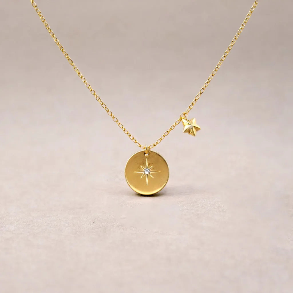 Collier Etincelle en acier doré avec pendentif rond orné d'une étoile et d'un cristal brillant, présenté face visible sur un fond beige. Verso personnalisable.