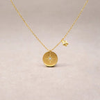 Collier Etincelle en acier doré avec pendentif rond orné d'une étoile et d'un cristal brillant, présenté face visible sur un fond beige. Verso personnalisable.