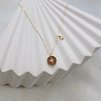 Collier Mon rêve en acier doré avec pendentif rond orné d'une étoile et d'un zircon, présenté face visible sur un fond beige. Verso personnalisable.