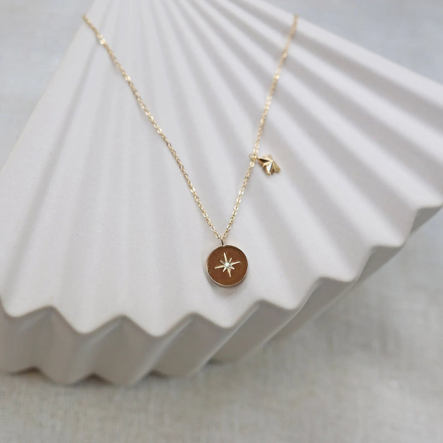 Collier Mon rêve en acier doré avec pendentif rond orné d'une étoile et d'un zircon, présenté face visible sur un fond beige. Verso personnalisable.