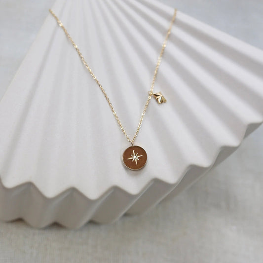 Collier Mon rêve en acier doré avec pendentif rond orné d'une étoile et d'un zircon, présenté face visible sur un fond beige. Verso personnalisable.