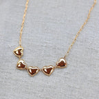Zoom sur le collier "Je suis là" de Visée, composé de cœurs personnalisables en acier doré, posé sur un fond beige texturé.