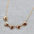 Zoom sur le collier "Je suis là" de Visée, composé de cœurs personnalisables en acier doré, posé sur un fond beige texturé.