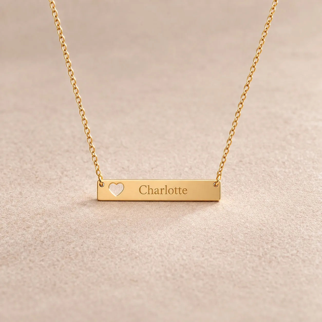 Collier doré personnalisable cœur gravé au nom de Charlotte – Douceur Visée Bijoux, posé sur fond beige texturé