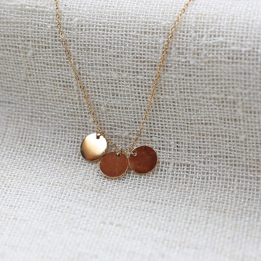 Collier "Inspiration" en acier inoxydable doré, composé de trois médaillons personnalisables, présenté sur un fond beige texturé.
