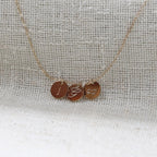 Collier "Inspiration" en acier inoxydable doré, composé de trois médaillons personnalisés d'initiales et dessin, présenté sur un fond beige texturé.