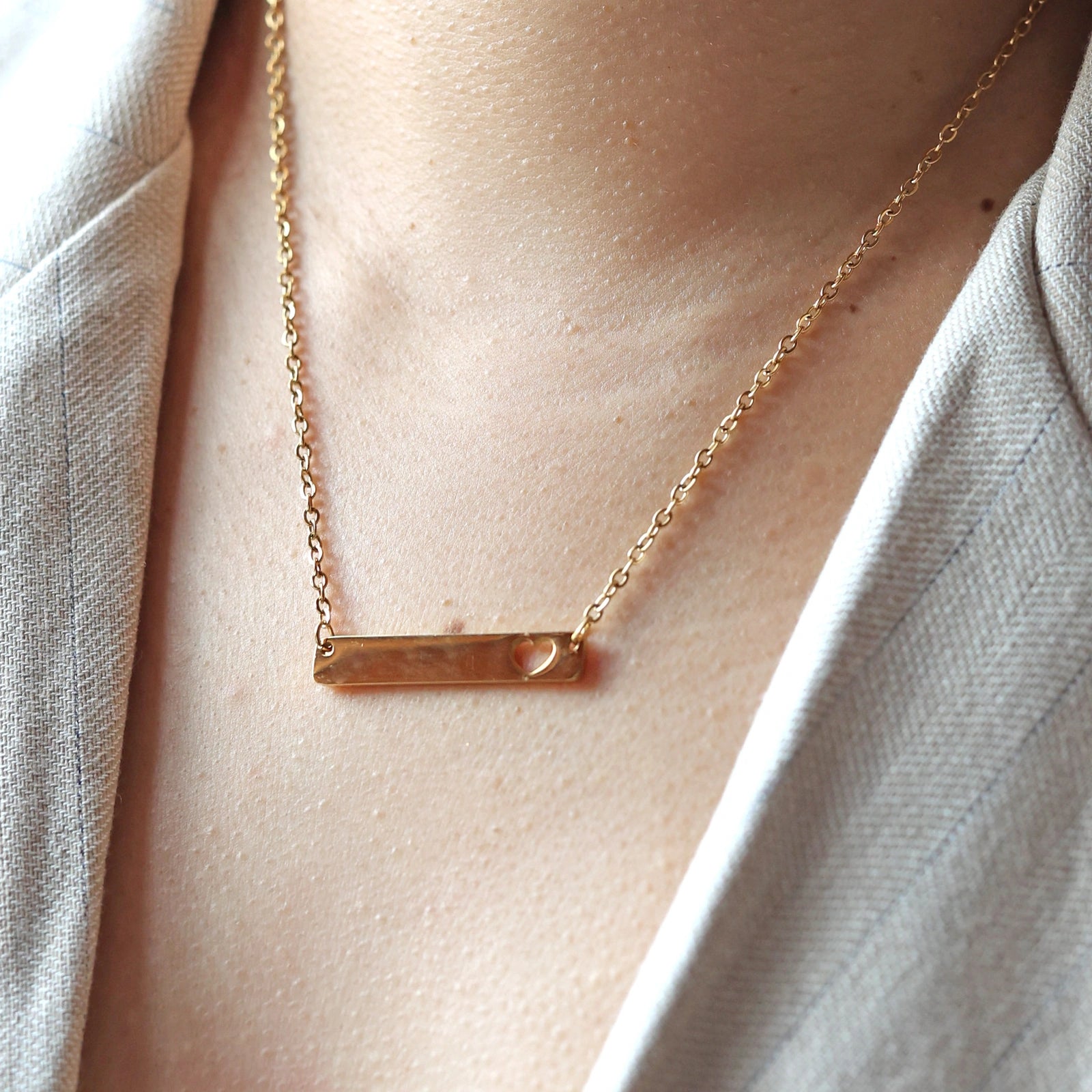 Collier plaque personnalisable en acier doré avec cœur découpé , porté sur un mannequin, photo en gros plan.