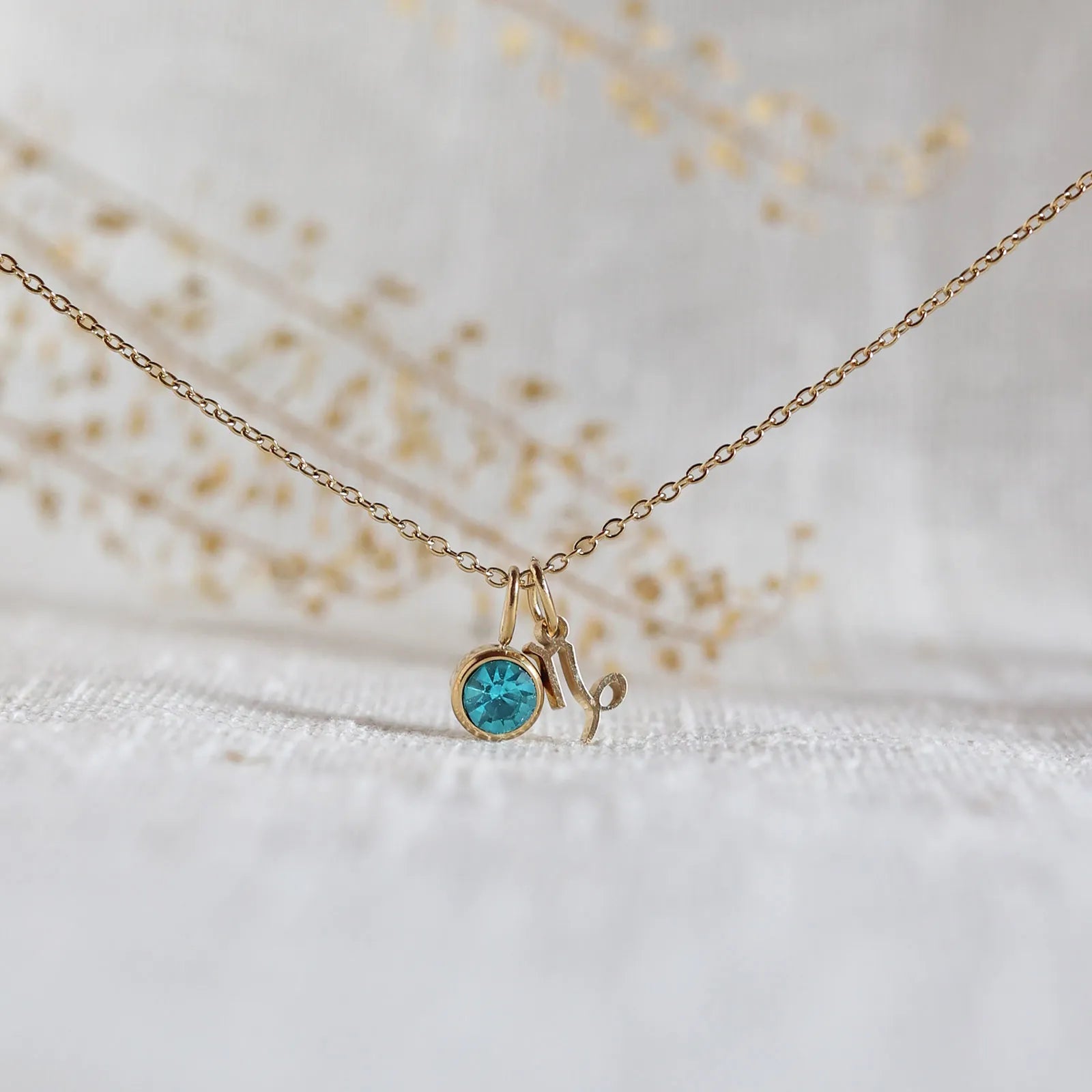 Collier "Mon identité" en acier doré, avec signe Capricorne et pierre bleue turquoise, délicatement suspendu sur une chaîne fine.